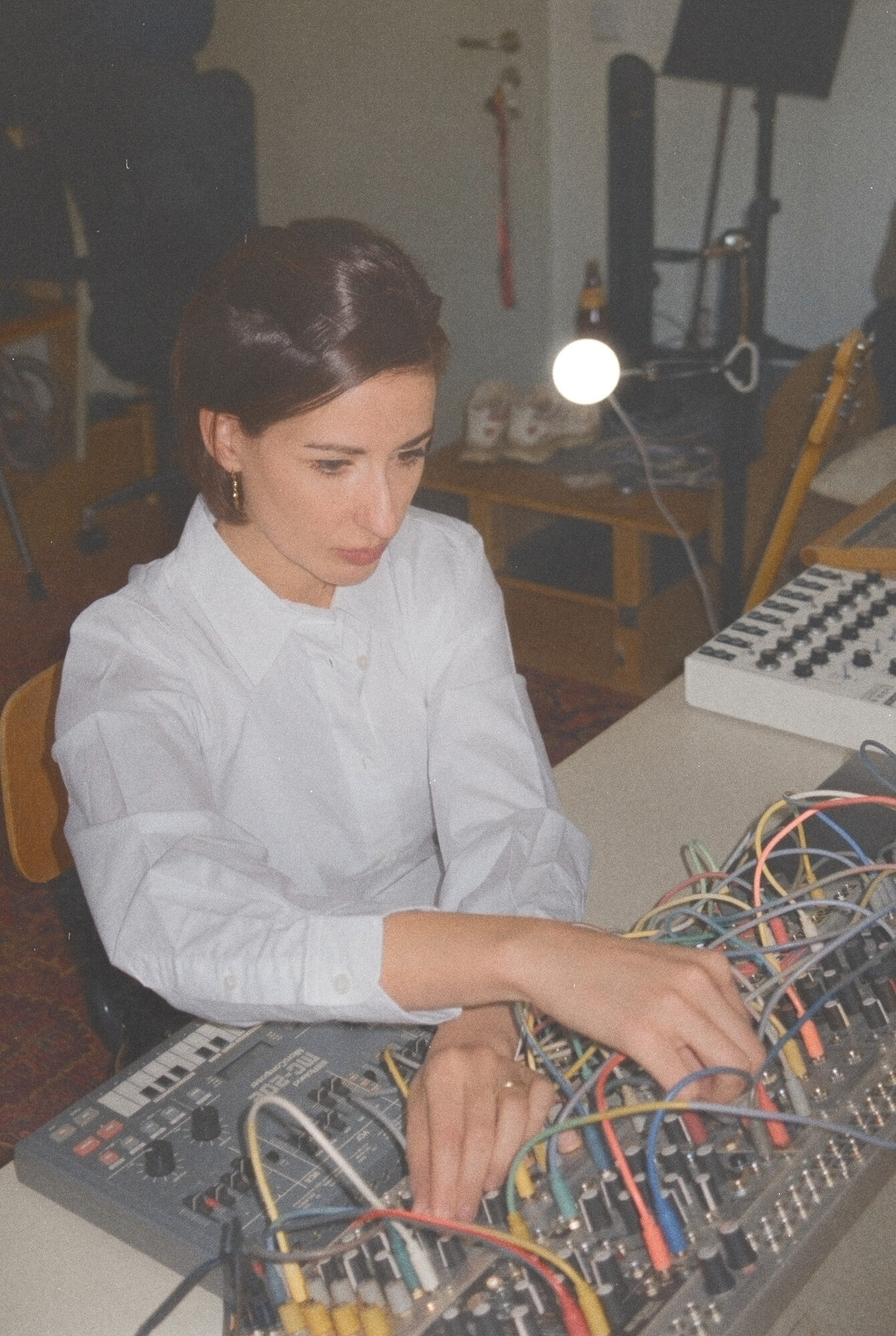 Maya Shenfeld seated in her studio among guitars and keyboards